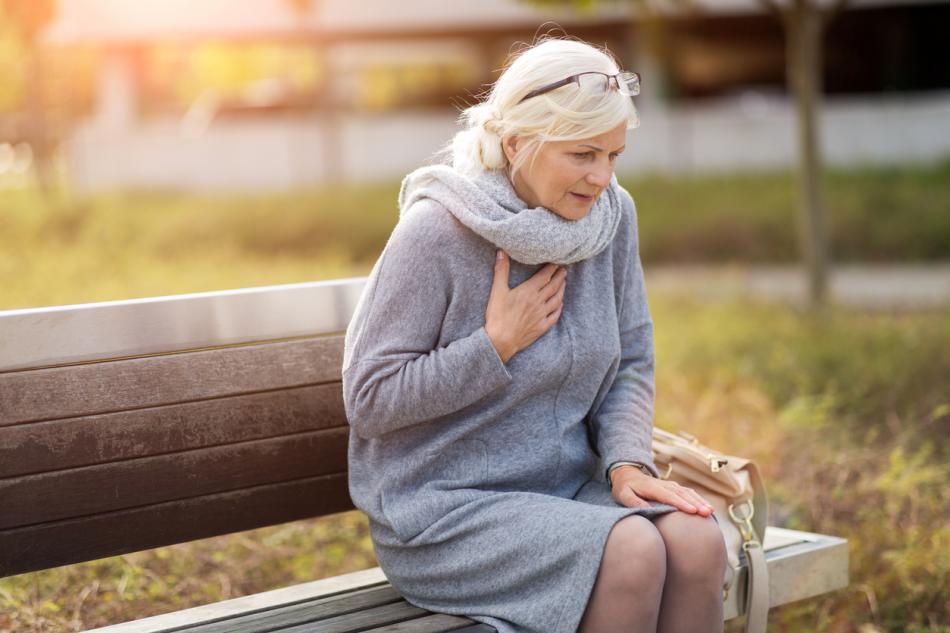 Elderly lady having chest pain sitting on a bench